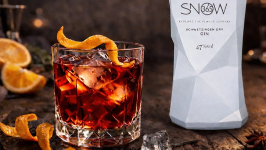 Negroni Cocktail mit Orangenzeste und Eiswürfeln neben SNOW365 Dry Gin Flasche auf rustikalem Holztisch