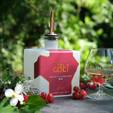 Weiße Ginflasche mit rotem Etikett der Limited Edition neben Tasting-Glas und roten Beeren im Garten.